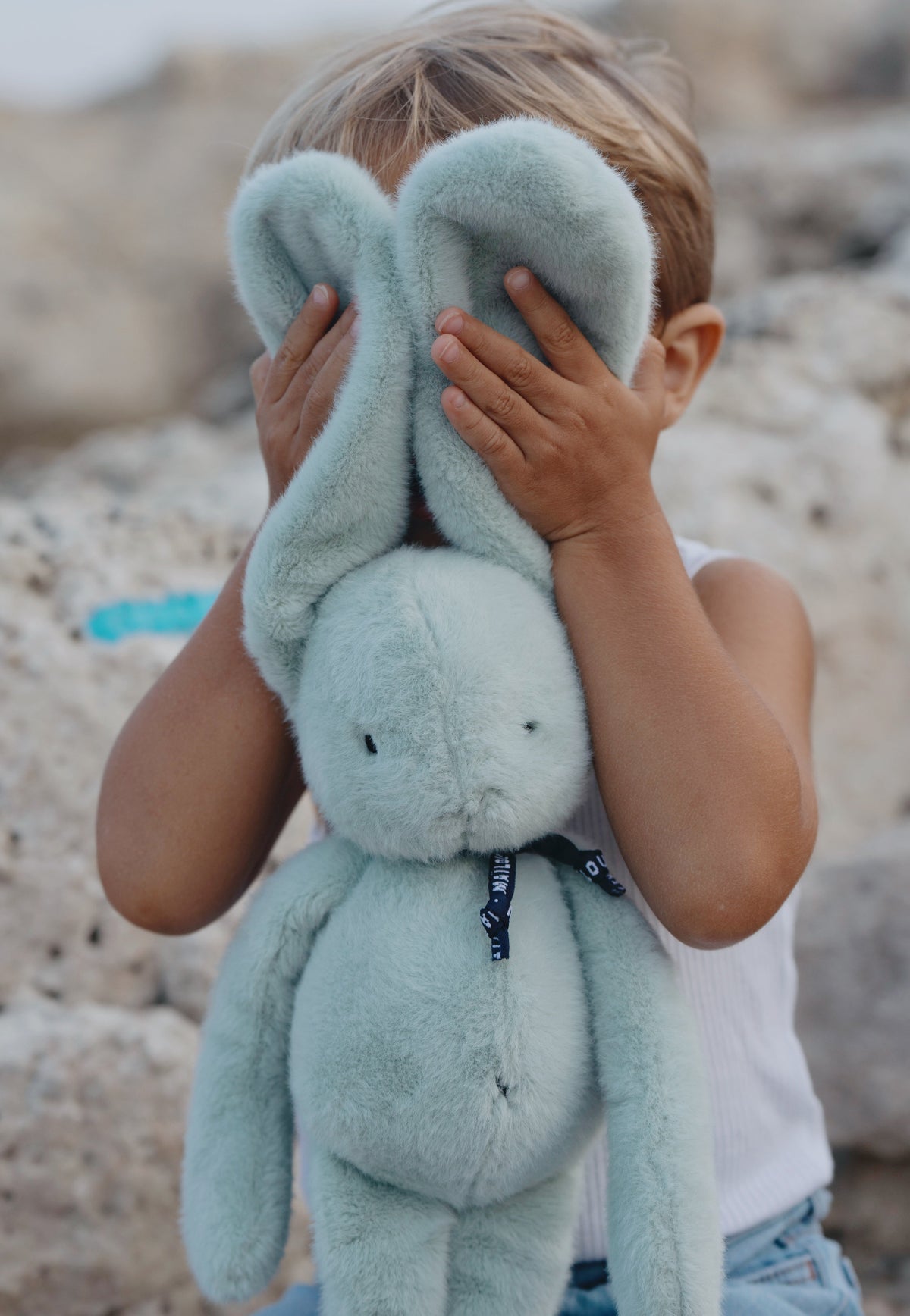 Petit garçon jouant à se cacher derrière les grandes oreilles d'une peluche lapin